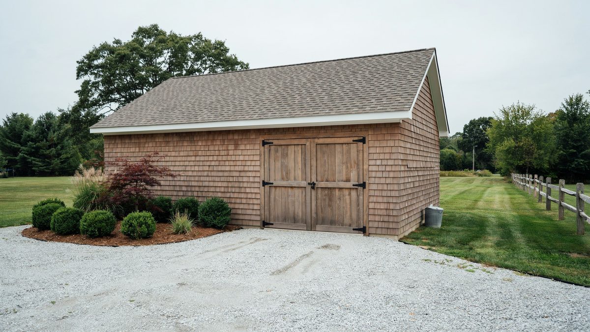 Cedar shingle garage shed with wood gate style doors on gravel drive