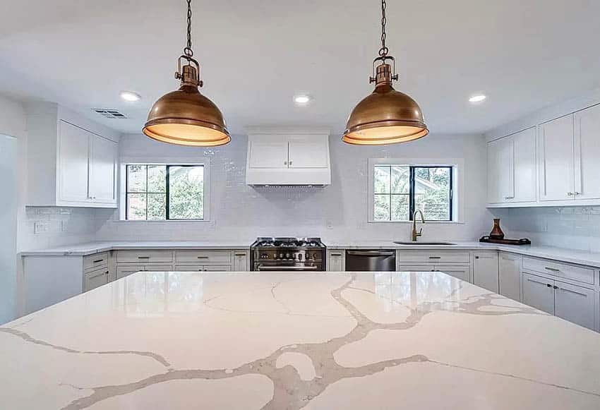 Kitchen with calacatta countertops, island, white cabinets and gold pendant lights