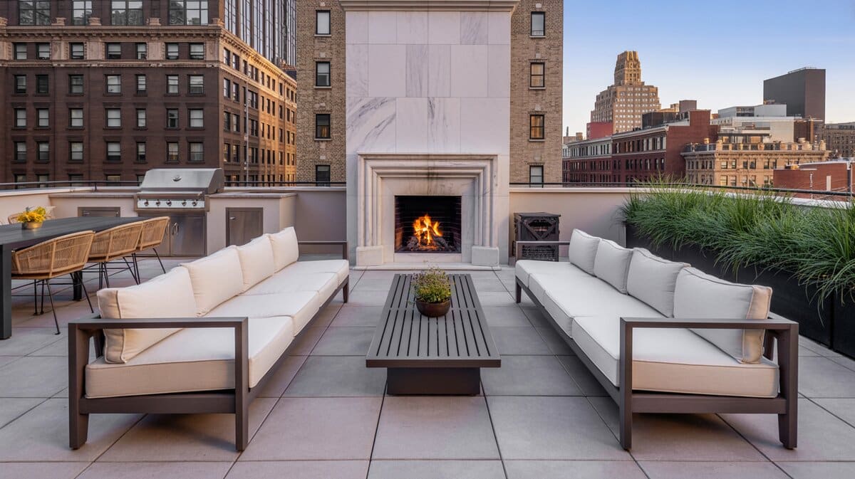 Luxury rooftop terrace with marble fireplace, white sofas, and grey tile pavers at dusk