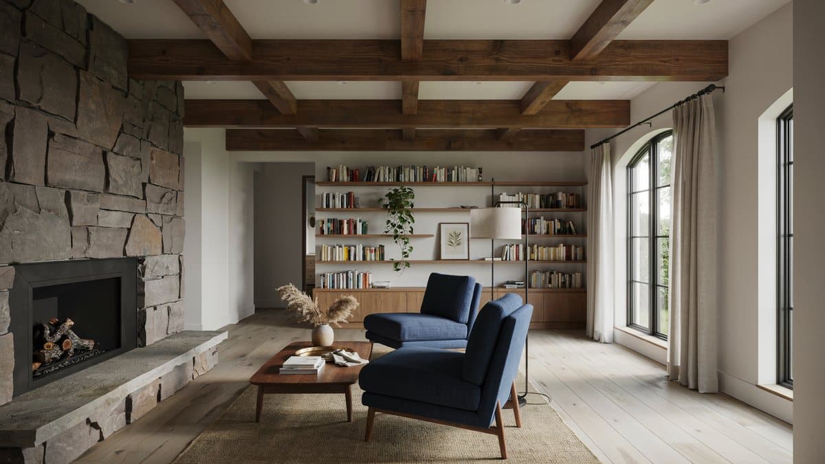 Living room with stone fireplace, exposed wood beams, bookshelves and blue armchairs