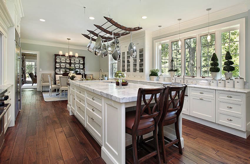 Cape cod kitchen with white shaker cabinets marble counters hardwood floors large windows