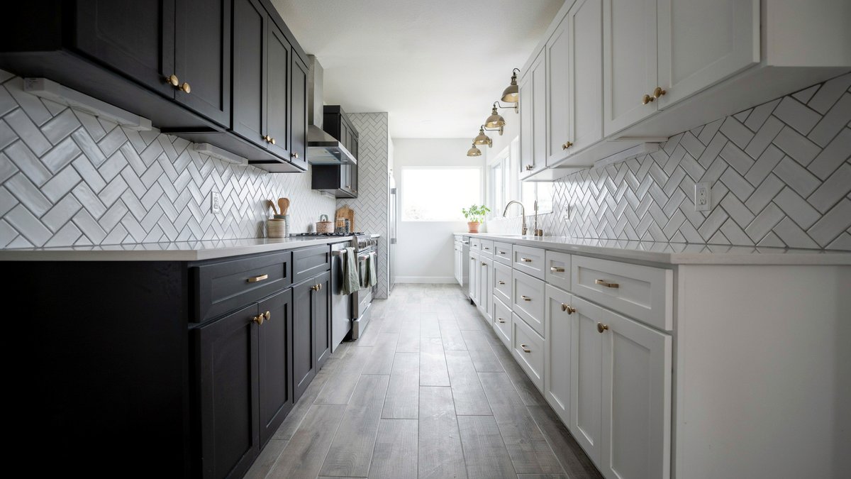 Galley kitchen with grey vinyl planks, black lower and white upper cabinets, gold hardware