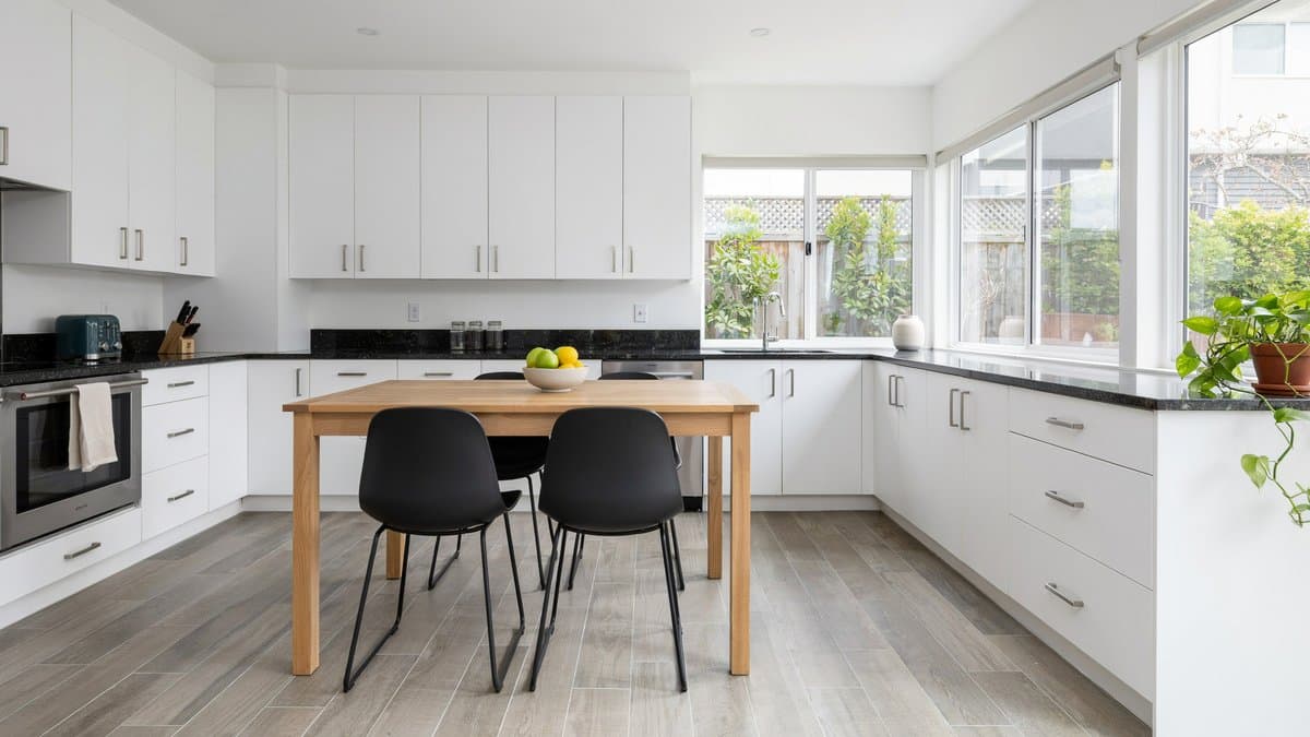 Kitchen with grey vinyl plank floors, white cabinets, black granite counters and oak island