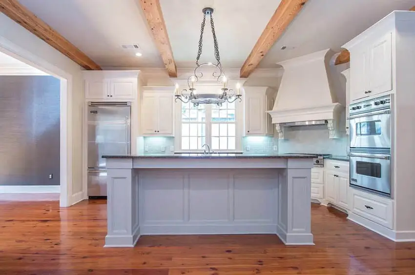 Kitchen with wood beams, wood plank flooring and white cabinets