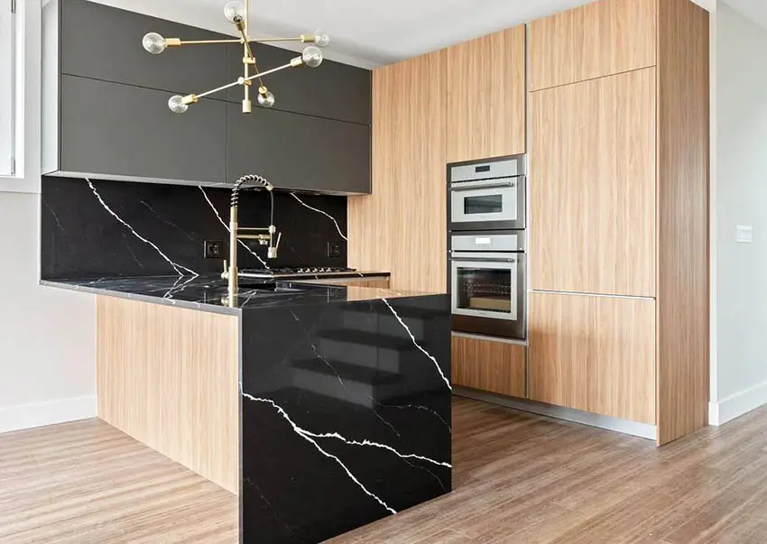 Kitchen with two tone cabinets, black waterfall quartz peninsula, and modern chandelier 