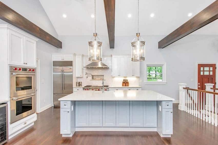 Open plan kitchen with white quartzite countertops white cabinets wood beam ceiling