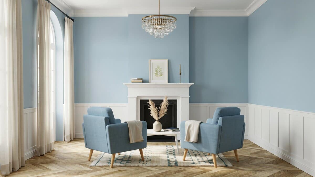 Powder blue walls with white wainscoting, twin armchairs, and a bright chandelier