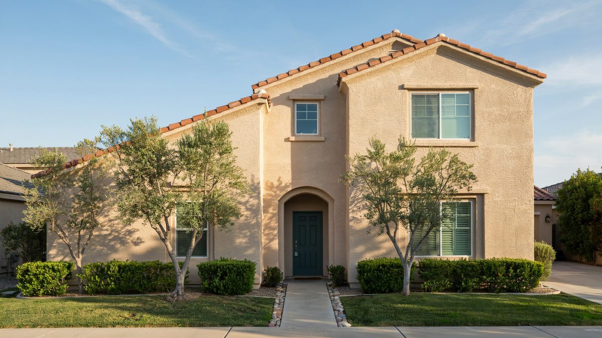 Two story sand colored stucco house with clay tile roof and arched entry