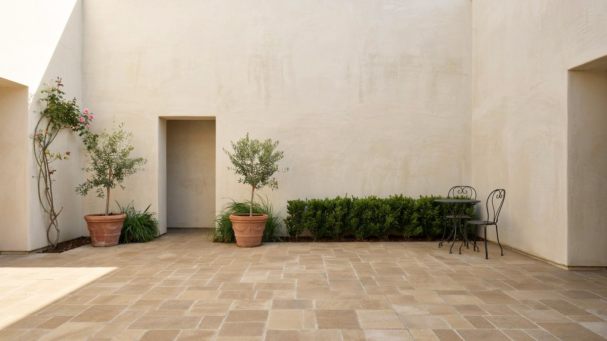 Cream textured stucco courtyard walls with potted olive trees and paver flooring