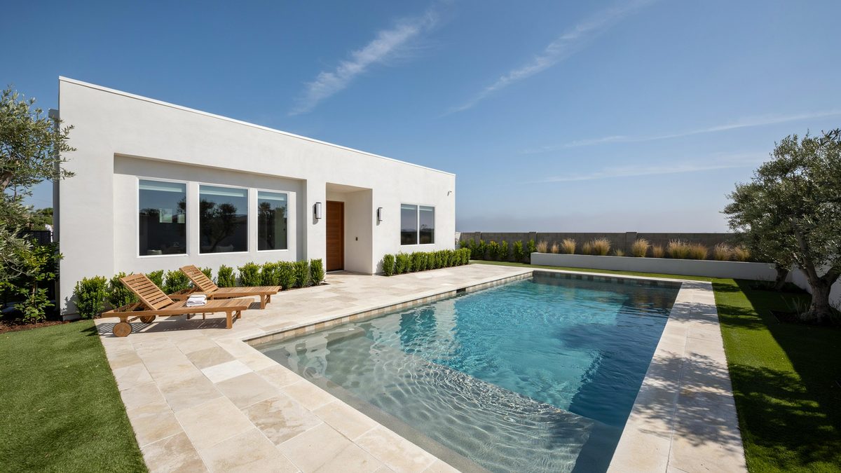 White stucco home beside a long rectangular pool with lounge chairs