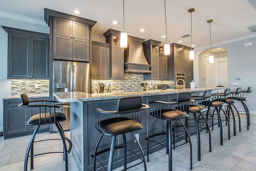 Kitchen with large floor tiles and dark gray cabinets with long island with 7 bar stools