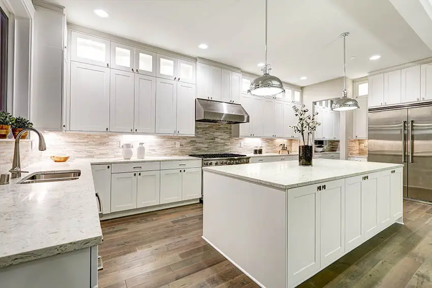 Kitchen with shaker cupboards, light color marble countertops chrome pendant lighting and wood floors