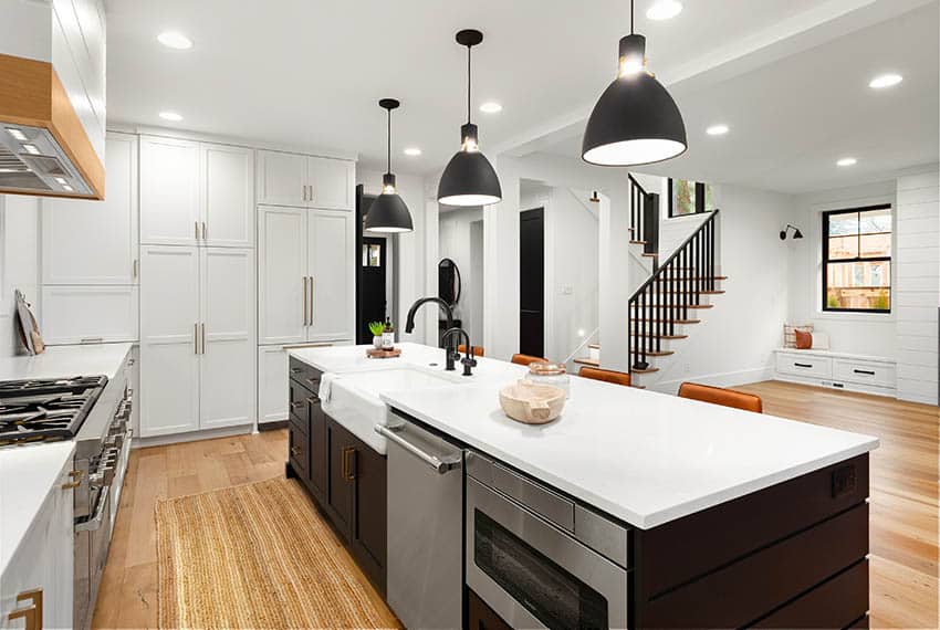 Contemporary kitchen with apron sink in island with white quartz countertops black pendant lights