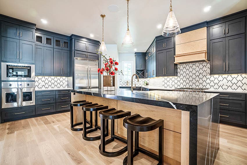 Kitchen with geometric backsplash, black cabinets, black quartz waterfall countertop and pendant lights 