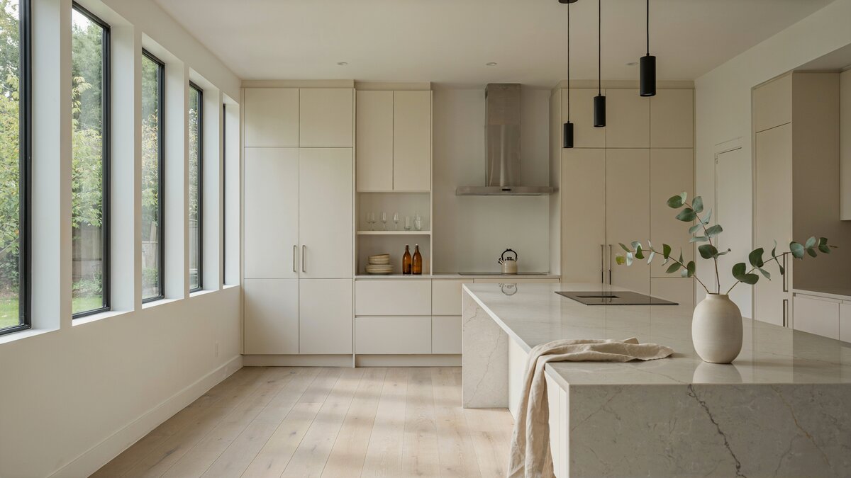 Contemporary kitchen with pale white oak flooring, a wall of windows, cream flat panel cabinets and a marble waterfall island