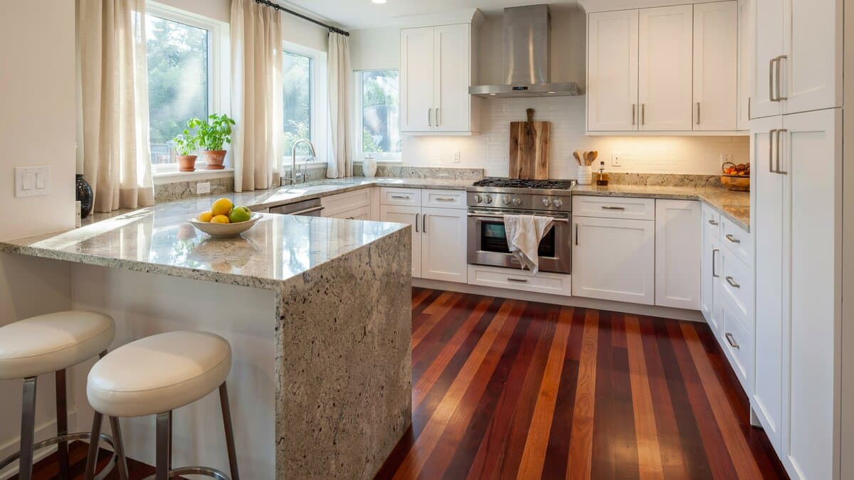 Kitchen with deep red jatoba Brazilian cherry flooring, white cabinets, a granite peninsula and two cream barstools