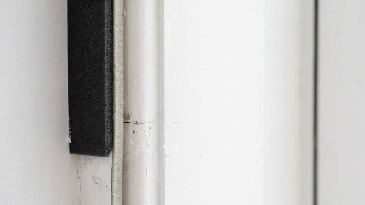 Black foam weatherstripping tape sealing the edge of a white door frame