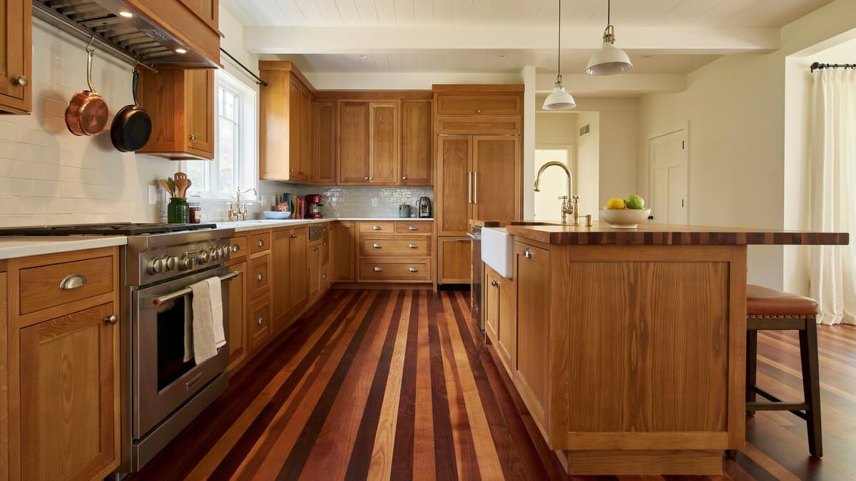 Traditional kitchen with striped tigerwood flooring, honey oak cabinets, copper pots on a rail and a butcher block island