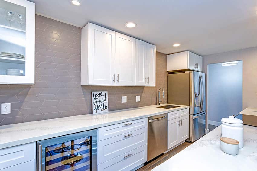 Contemporary galley style basement kitchen with shaker cabinets white quartz countertops tile backsplash