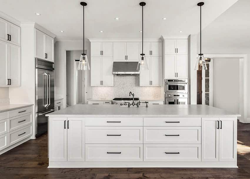 Kitchen with quartz tile backsplash, white shaker cabinets and pendants