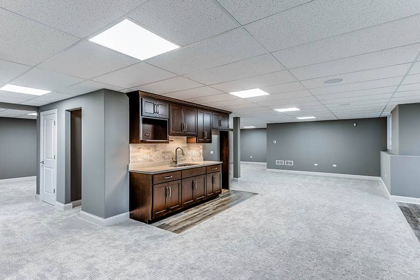 Small kitchen in the basement with alderwood material, beige slate backsplash and grey floor carpeting