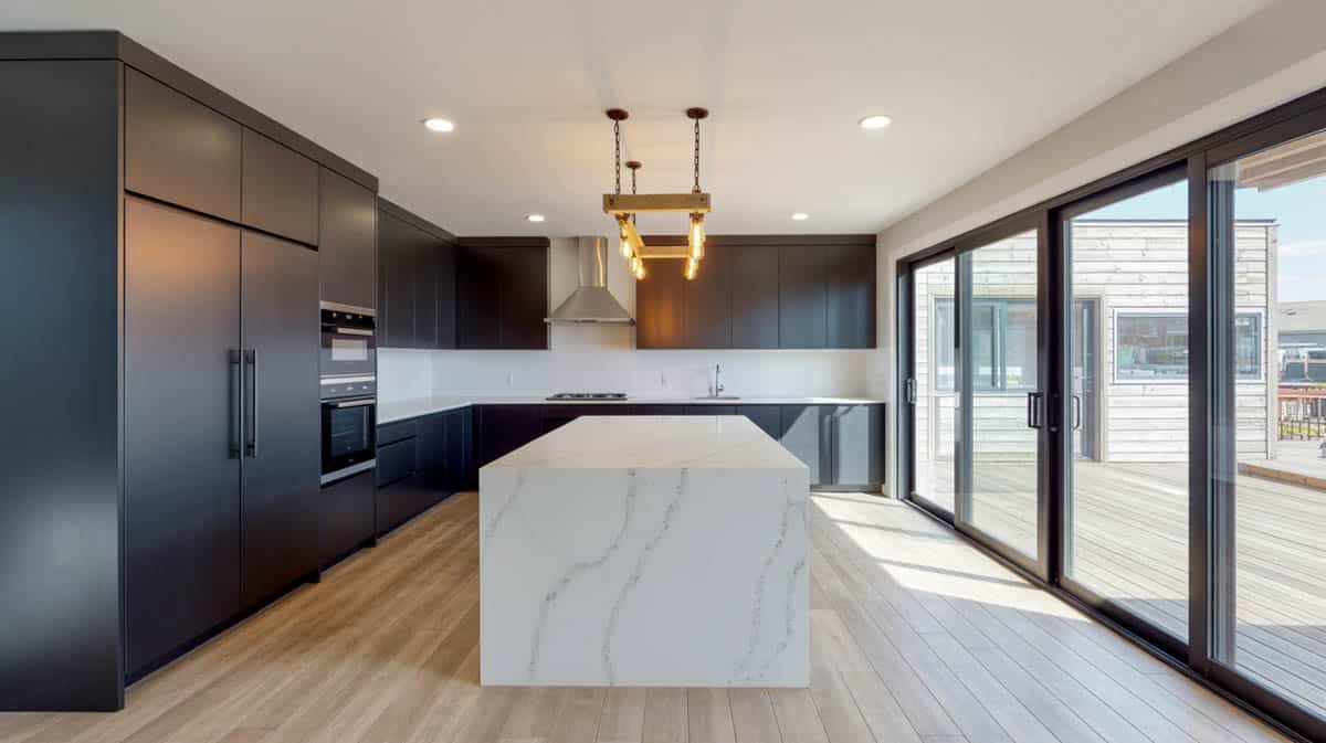 Ink-black matte flat-panel kitchen with a dramatic white waterfall quartz island and large sliding glass doors