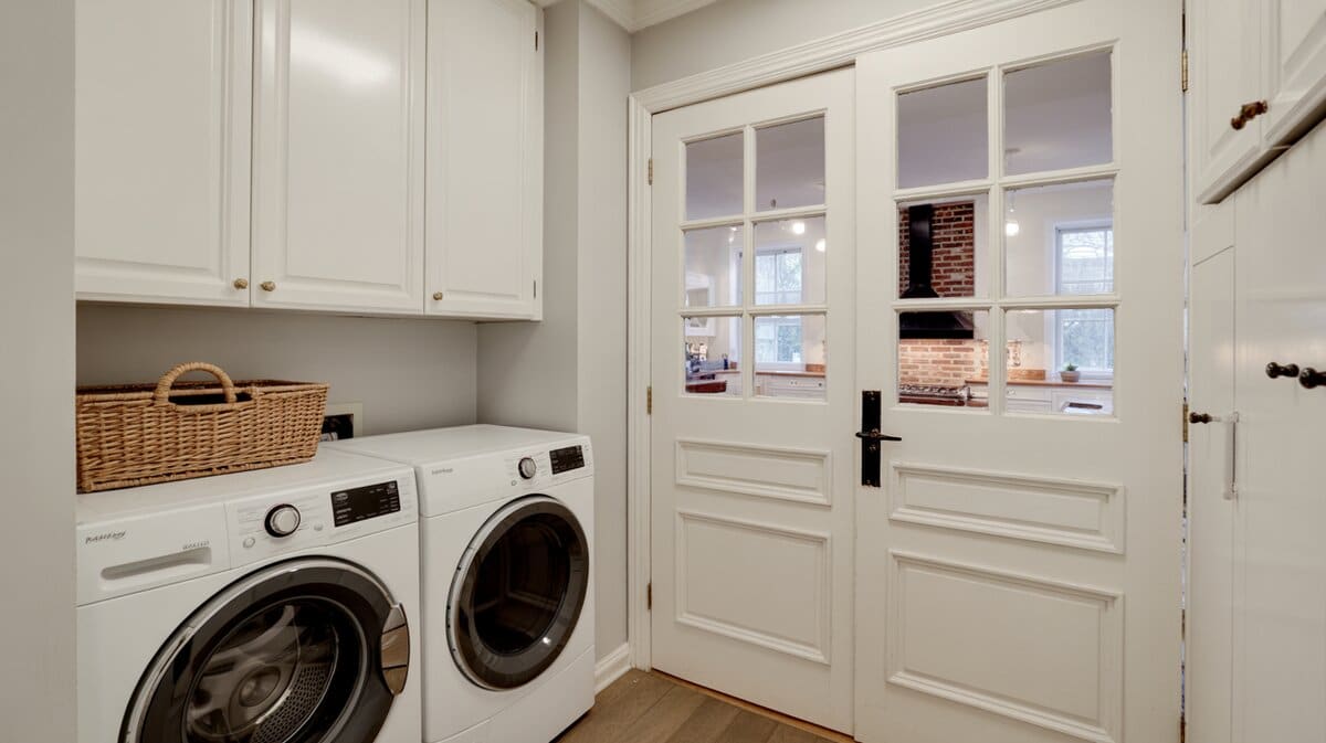 White laundry room with Dutch door top half open revealing kitchen view with exposed brick wall