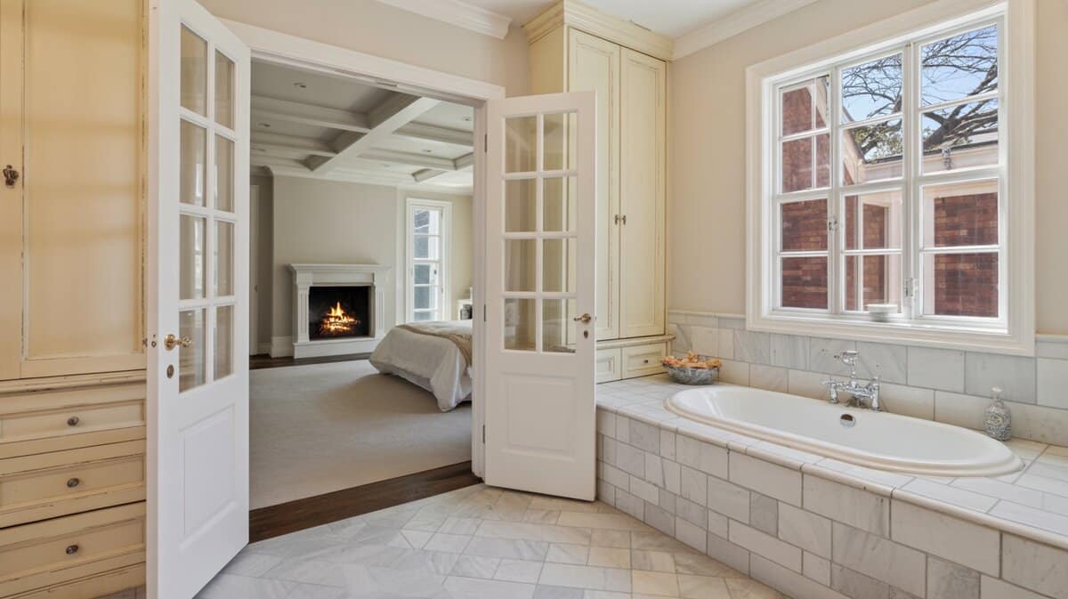 Luxurious master bathroom with French door open to bedroom featuring marble floors oval soaking tub and two-sided fireplace