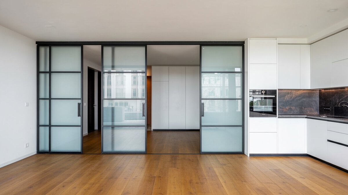 Modern open-plan apartment with large frosted glass sliding room divider on ceiling track beside white kitchen