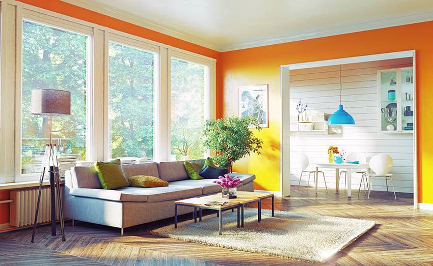 Orange painted living room withgreen accent pillows on neutral couches