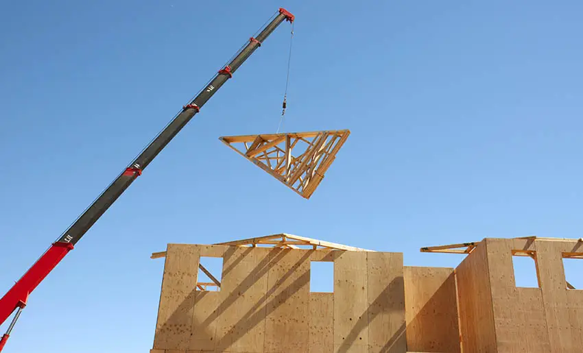 Crane lifting wooden roof truss to house