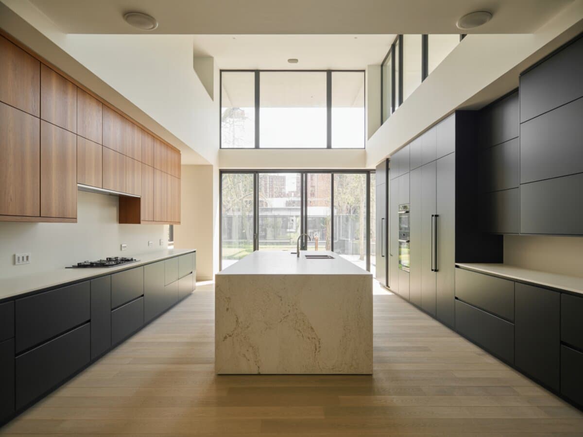 Ash wood and charcoal cabinets flank a creamy stone island under soaring double-height windows