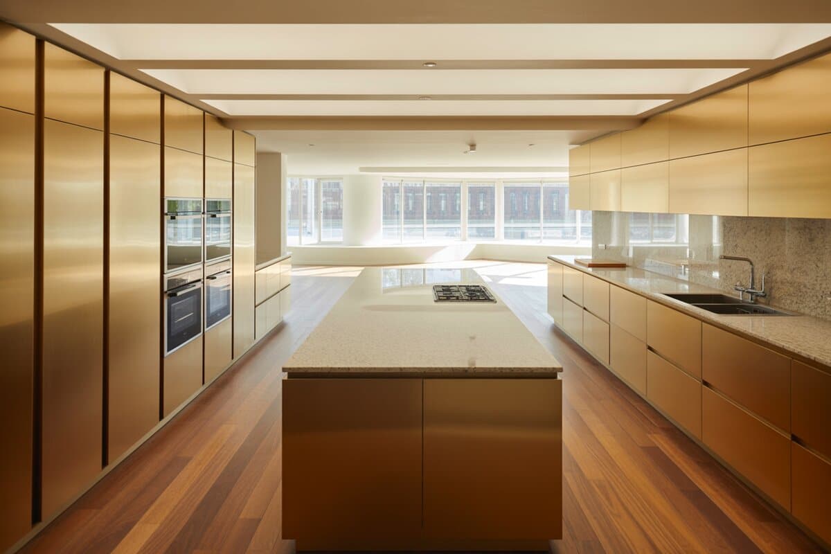 Glossy golden cabinets surround a granite-topped island with stainless ovens and city-view windows