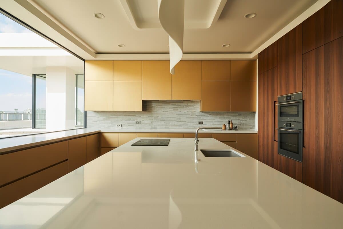 Golden cabinets and walnut tower meet a white solid-surface island with linear stone backsplash