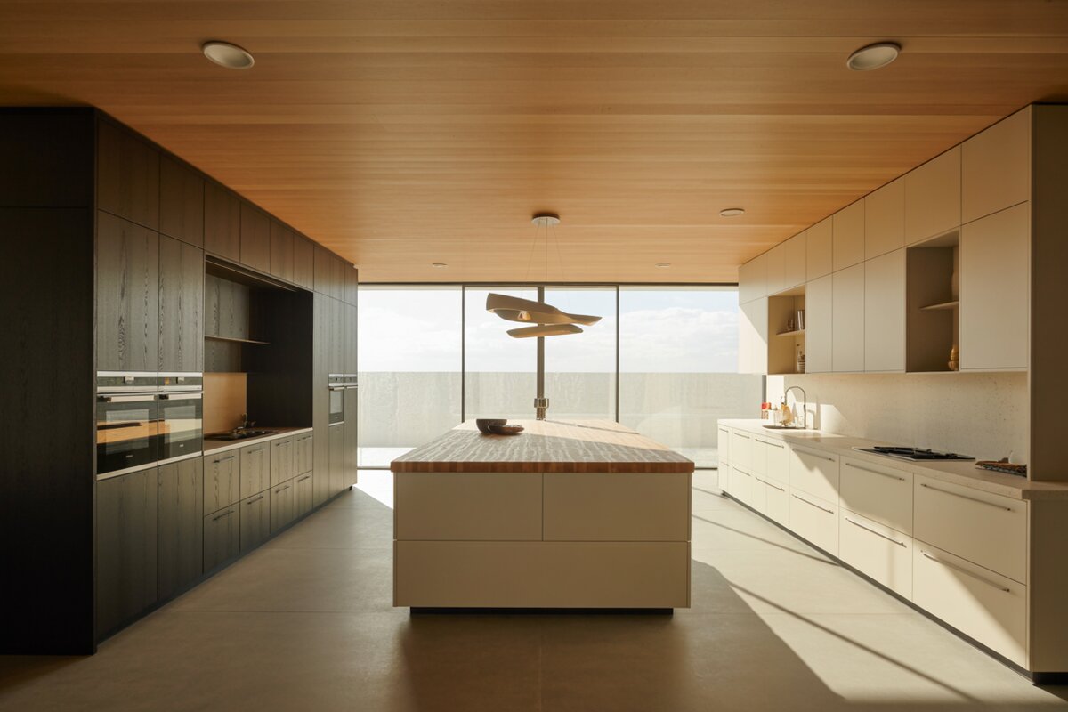 Charcoal and cream cabinets pair with a butcher-block island beneath a warm wood-plank ceiling