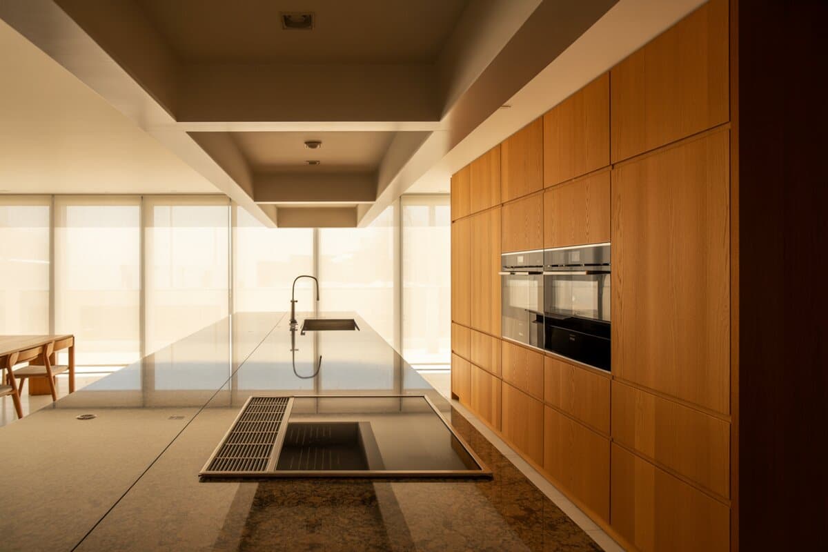 Oak cabinetry lines one wall beside a granite island with built-in cooktop and floor-length sheers