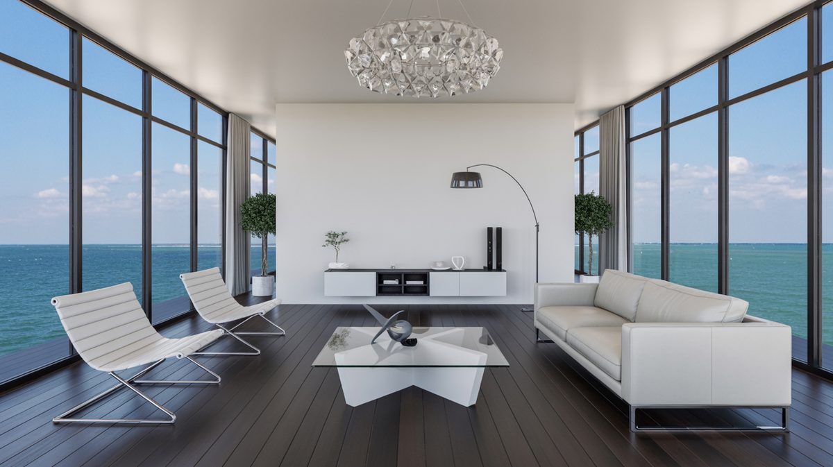 Bright modern masculine living room with floor-to-ceiling glass walls, ocean view, white leather sofa, and statement crystal chandelier