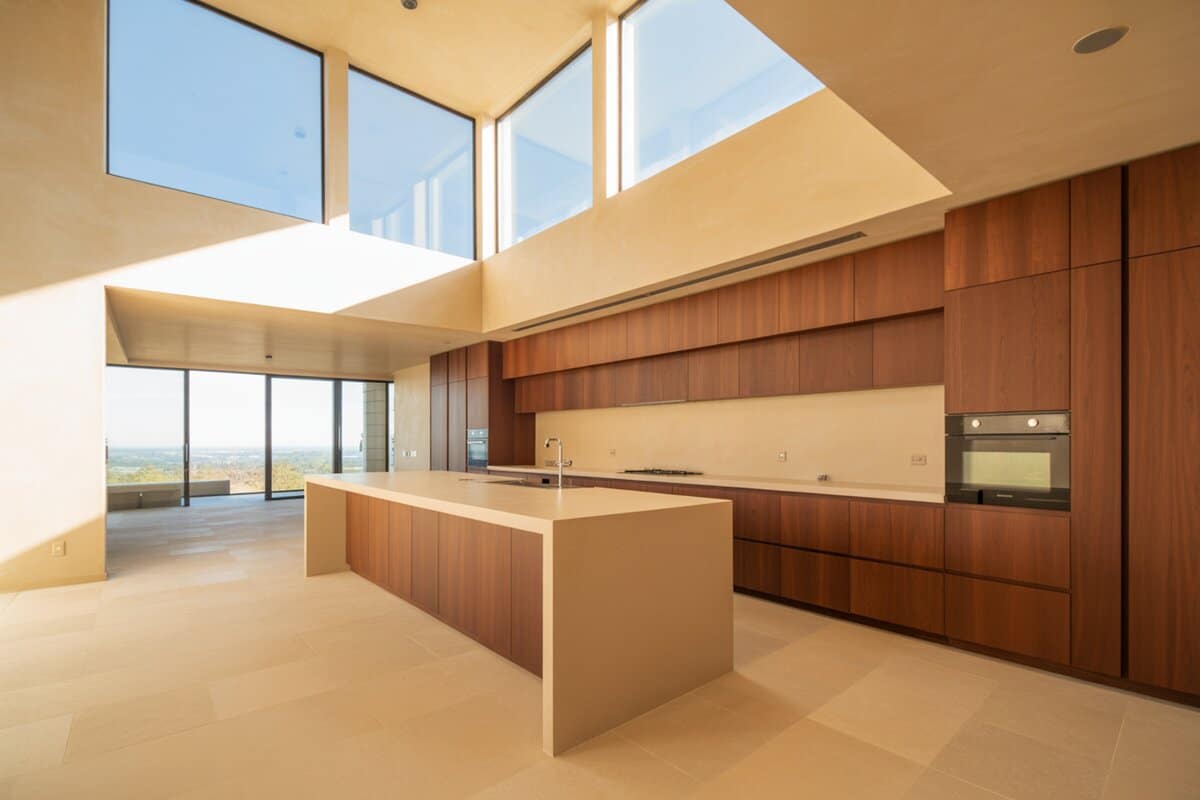 Mahogany cabinets line a creamy island below clerestory windows in a sunlit double-height room