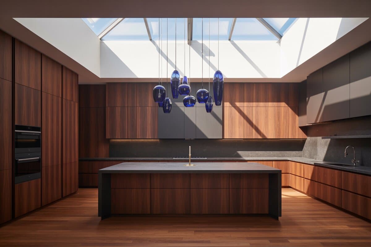 Walnut cabinets surround a dark island lit by cobalt glass pendants under a skylight