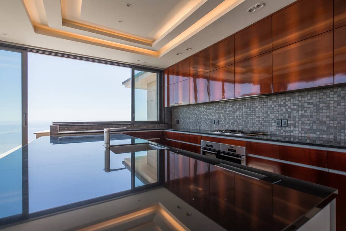 Glossy cherry cabinets and black granite counters face an ocean view through sliding windows