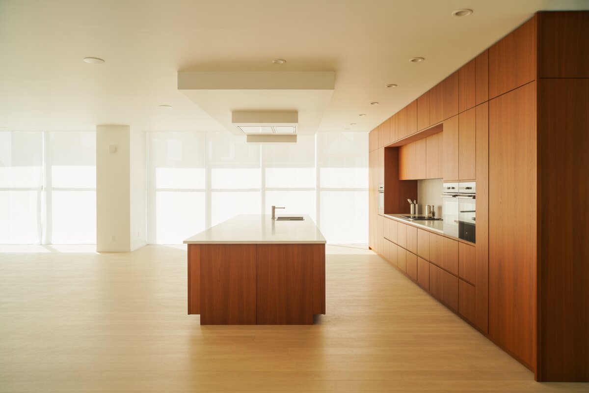 Teak cabinets line one wall behind a quartz-topped island over pale maple flooring