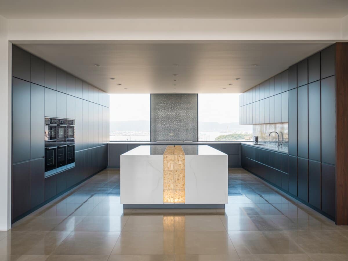 Slate blue cabinets flank a white island with backlit onyx panel and silver mosaic wall