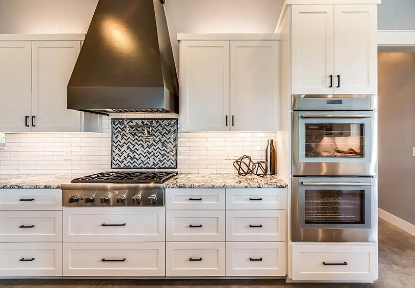 Kitchen withc backsplash mosaic tile inlay and white cabinets with black handles