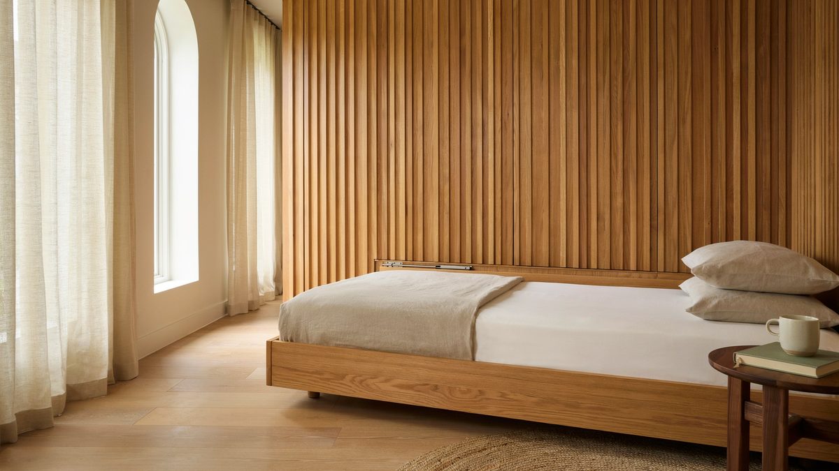 Low profile wood platform bed against a slatted oak wall and arched window