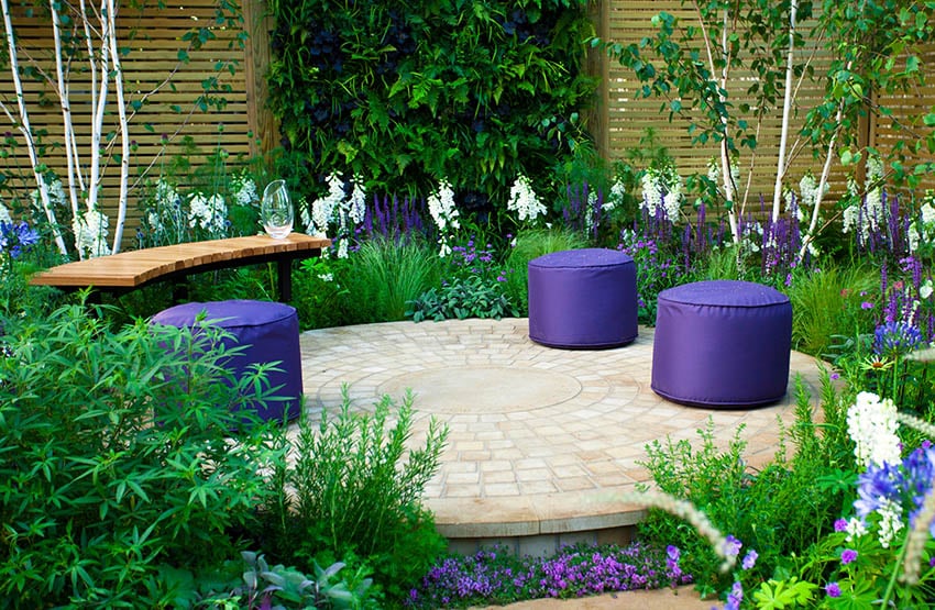 Circular raised paver patio with curved wood bench and flowering plants