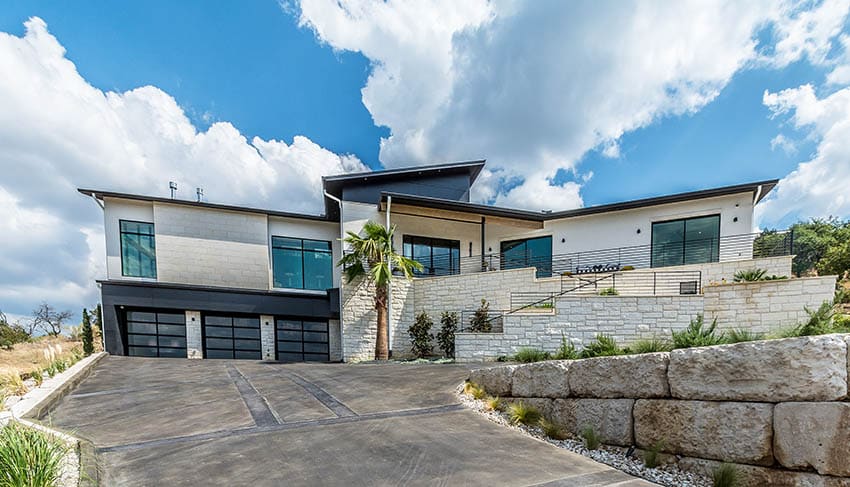 Modern house with sloped concrete driveway 3 car garage and stone wall