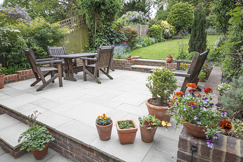 Raised brick and concrete patio with wood dining table potted plants