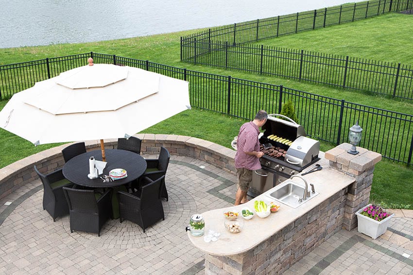 Raised brick paver patio with circular design outdoor kitchen and dining table