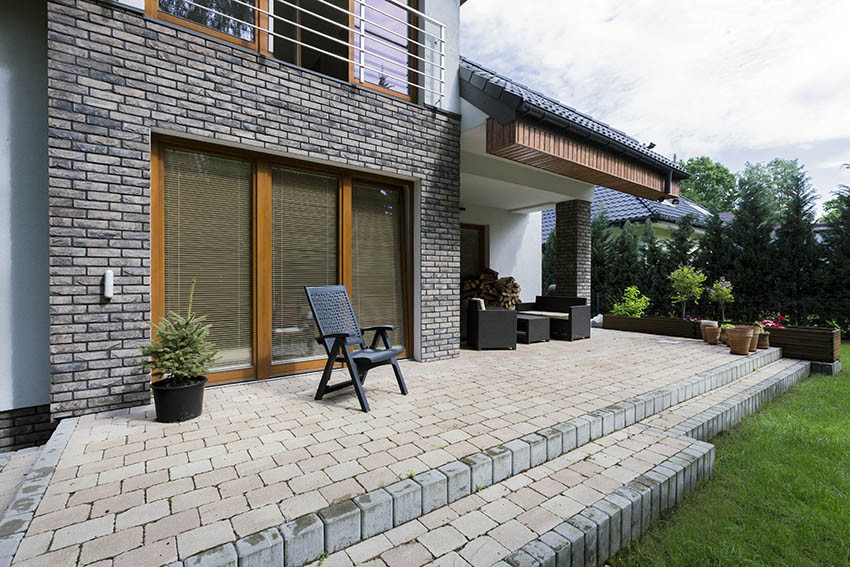 Raised paver patio in backyard with steps and covered ceiling