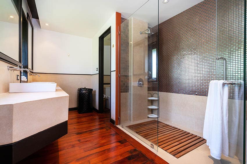 Bathroom with teak wood floors, shower area, tile wall, vanity, sink, and glass divider